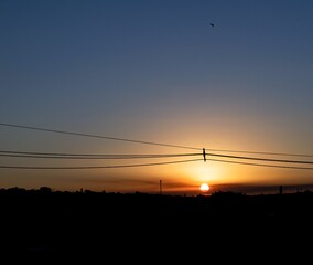 Por do sol em uma pequena cidade com fios de eletricidade cortando o ceú.