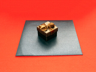 Gift box in bronze color with a bow and a black craft envelope on a red background