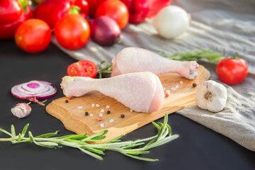 Raw chicken legs with rosemary, tomatoes, and spices on a black wooden background. Creative atmospheric decoration
