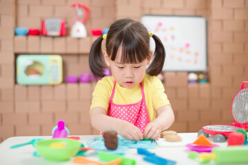 Fototapeta premium young girl pretend play food preparing role against cardboard blocks kitchen background