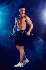 Fototapeta na wymiar Athletic man flexing muscles in studio on dark background with smoke. Strong bodybuilder with perfect abs.