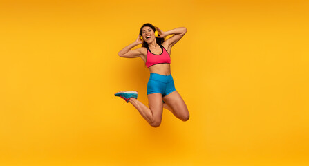 Fototapeta na wymiar Sport woman jumps on a yellow background and listen to music. Happy and joyful expression.