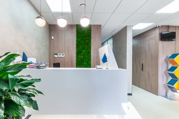 White reception corner with high-tech office equipment. The room decorated with the moss wall and a...