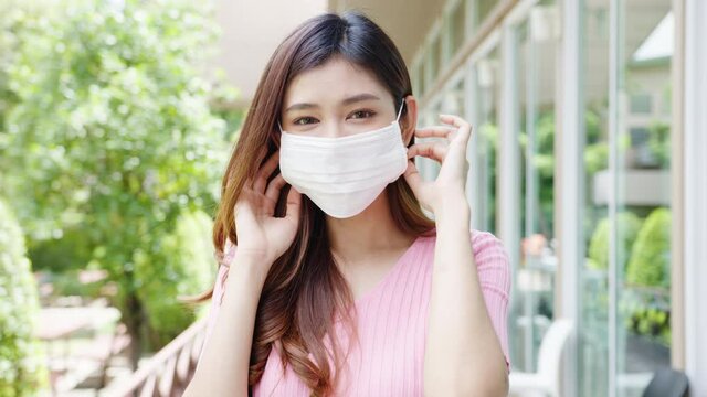 Young Asia businesswoman wear protective face mask looking at camera outside during Covid-19 coronavirus health crisis in street in city. Lifestyle new normal after corona virus and social distancing.