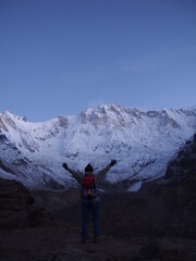 A climber raises her arms in front of a snow-covered rock in the early morning, ABC (Annapurna Base Camp) Trek, Annapurna, Nepal