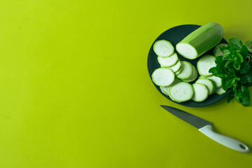 zucchini sliced ​​on a plate, mint, knife, on a green background.green monotonous image with zucchini
