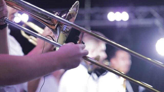 The musician plays the trombone with the band on stage, close up from the side.