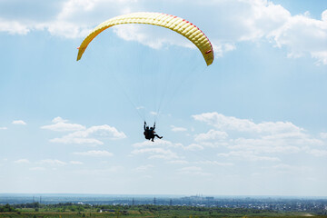 Yellow Paraglider tandem instructor with a tourist flying into the sky with clouds on a sunny day