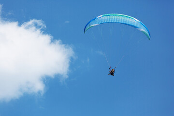 Blue Paraglider flying into the sky with clouds on a sunny day