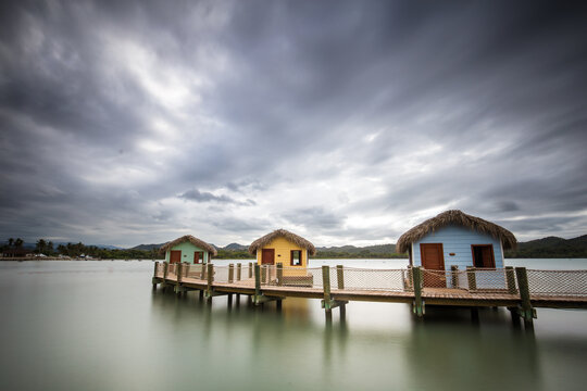 View of cabins on wooden pier in sea against cloudy sky