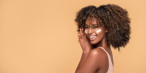 Young afro woman with moisturizer on face. - obrazy, fototapety, plakaty