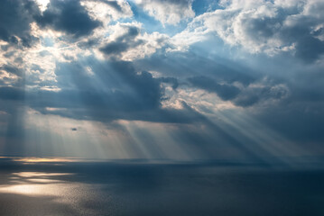 Sun rays through dark clouds over the sea with reflection