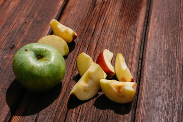 Delicious and healthy food for healthy and active people. One whole green Apple and a red Apple cut into pieces lie on the wooden kitchen table.