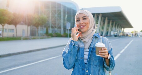 Close up of Arabic young beautiful woman in hijab talking on mobile phone at street. Urban...