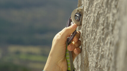 CLOSE UP: Rock climber clips a carabiner into a bolt screwed into the cliff.