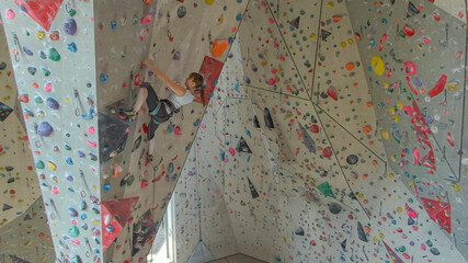 DRONE: Young female rock climber climbing in a cool indoor training center.