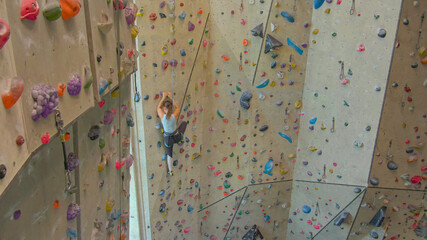 DRONE: Fit young woman scales a challenging route in an indoor climbing center.