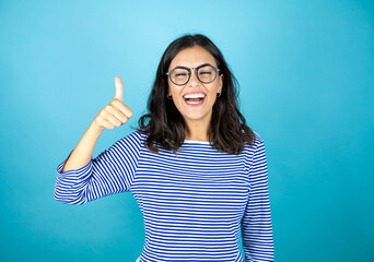 Pretty woman wearing glasses standing over insolated blue background smiling and doing the okay signal. positive person