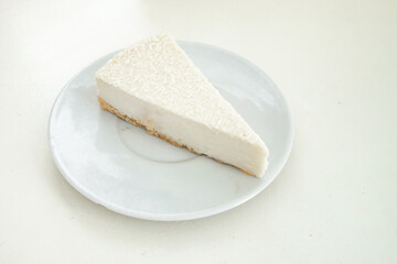 1 piece of cheesecake on a white saucer on a white table on a white kitchen with natural light