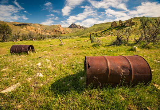 View of rusty barrels on grassy landscape against cloudy sky