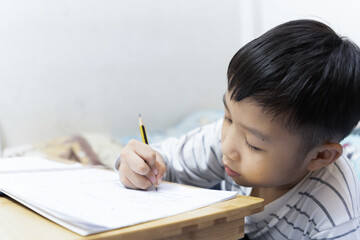 Home school and new normal lifestyle concepts.Asian boy studying through online media and do homework at home due to social distance policy to prevent the spread of the coronavirus(Covid-19)