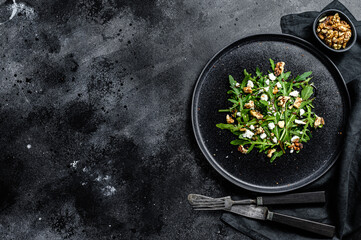 Healthy salad with arugula, goat cheese, nuts and vinaigrette sauce. Black background. Top view. Copy space