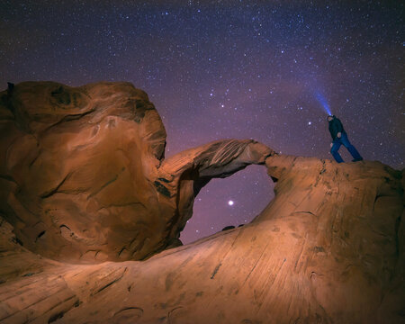 Low angle view of man standing on arch rock with his headlamp shining towards stars in sky