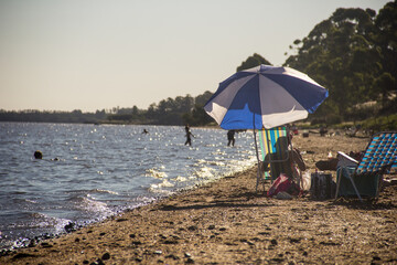 sombrilla en la playa y chicos jugando en el agua
