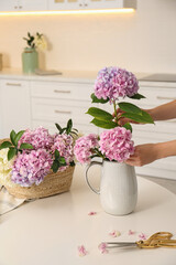 Woman making bouquet with beautiful hydrangea flowers at table indoors, closeup. Interior design element