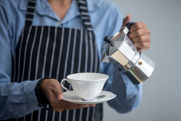 The young barista poured coffee into a white glass to serve it to the customer.