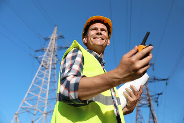 Professional electrician with portable radio station near high voltage tower