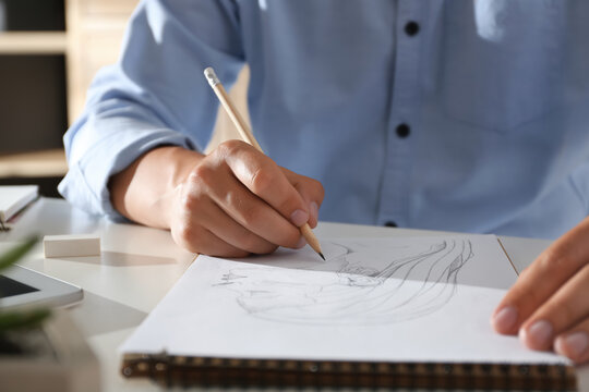 Man drawing portrait with pencil in notepad at table, closeup