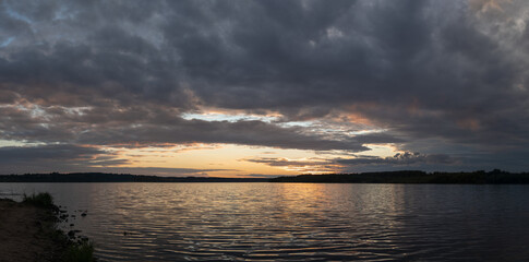 Panorama of the wide river after sunset. Picturesque panoramic view of the wide river after sunset. The natural colors of the sunset are reflected in ripples on the wide surface of the river.