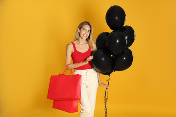 Happy young woman with balloons and shopping bags on yellow background. Black Friday Sale
