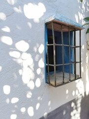 window with a lattice on the white wall of the house with sunny glare and a shadow of trees