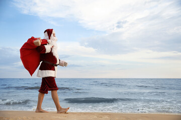 Santa Claus with bag of presents on beach, space for text. Christmas vacation