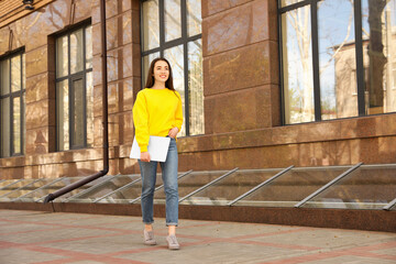 Happy young woman with laptop walking outdoors