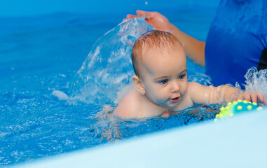 Fototapeta na wymiar Coach teaches the baby to swim in the pool. baby splash in the water in the pool. The concept of a healthy