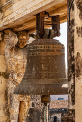 Obraz premium Leon, Nicaragua - November 27, 2008: Cathedral of Assumption, Asuncion.. Closeup of heavy dark metal old bell hanging in part of yellow stone towers, flanked by statue of man supporting beam. 