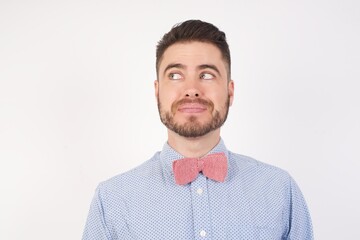 European man dressed in formal shirt and bow tie poses against white studio background, looking aside into empty space thoughtful