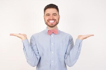European man dressed in formal shirt and bow tie poses against white background holding two palms copy space