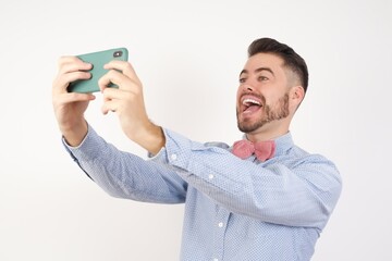 Close-up portrait European man dressed in formal shirt and bow tie poses against white studio...