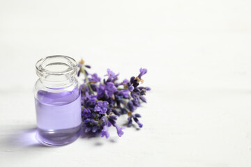 Obraz na płótnie Canvas Bottle of essential oil and lavender flowers on white wooden table. Space for text