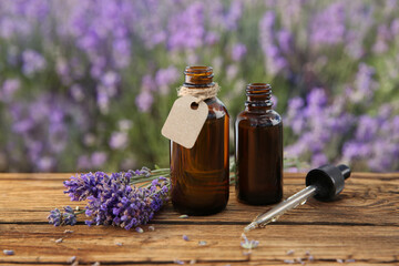Bottles of natural essential oil, pipette and lavender flowers on wooden table