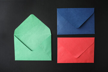 Colorful paper envelopes on black background, flat lay