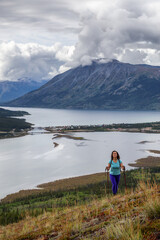 Fototapeta premium Adventurous Girl Hiking up the Nares Mountain during a cloudy and sunny evening. Taken at Carcross, near Whitehorse, Yukon, Canada.