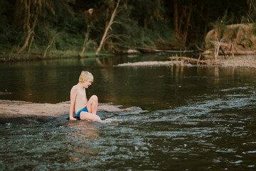 Boy sitting on rock while swimming in natural swimming hole in central New South Wales, Australia