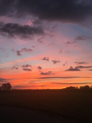Brilliant sunset against stark country landscape that glows in yellows, oranges, peaches, light blue against pink, violet, gray and black clouds. 