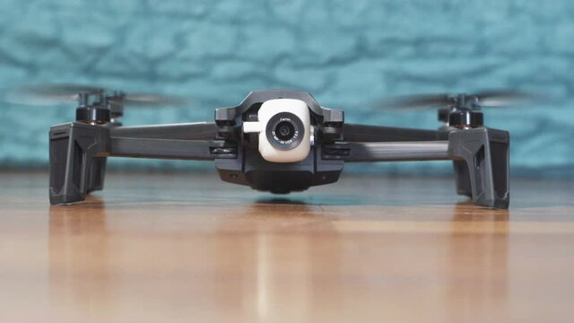 Launch of a black and white drone on parquet floor at home in slow motion. Causing wind in the background