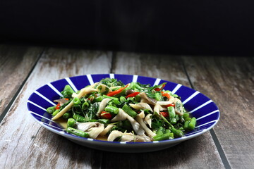 Traditional fried and stirred chopped mushroom with cutting green bean and chilly seasoning with pepper and soy sauce on the plate. Famous spicy vegetarian menu in Asia restaurant. 
